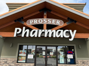 Cheerful female pharmacist offering help in choosing at counter in pharmacy