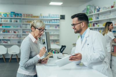 Happy senior woman customer buying medications at drugstore while talking with a male pharmacist